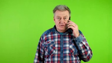 Günlük kıyafetlerle yürüyen ve akıllı telefonuyla konuşan kıdemli bir adam. Modern insanların hayatlarıyla iletişim kurma teknolojisi. Yeşil ekran. Krom anahtar.