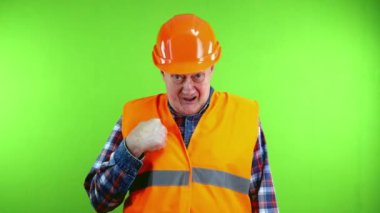 Başlık takmış kıdemli inşaatçı çalışmayı reddediyor, el sallıyor ve baş parmağını sallıyor. Olgun işçi olumsuz tepki veriyor ve işten memnun değil. Yeşil ekran, krom anahtar.
