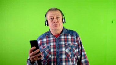 Komik, mutlu, son sınıf öğrencisi müzik kulaklıkları dinliyor ve şarkı söylüyor. Düşüncesiz, olgun bir insan günlük giysiler içinde yürüyor ve hayatından zevk alıyor. Yeşil ekran, krom anahtar.