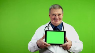 Gülümseyen kıdemli doktor tıbbi haberler veya reklamlar için dijital tablet tutuyor. Olgun sıhhiyeci sosyal medyada yeni tıbbi teknolojilerin veya ilaçların sunumunu yapar. Yeşil ekran. Krom anahtar.