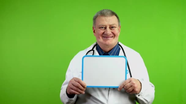 Sorrindo Médico Sênior Mantém Mesa Branca Para Notícias Médicas Publicidade — Vídeo de Stock