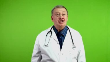 Gülümseyen kıdemli doktor başparmağıyla evet işareti yapıyor ve kameraya bakıyor. Sağlık hizmetleri yeşil ekranında başarıya ulaşan olgun bir doktor. Krom anahtar.