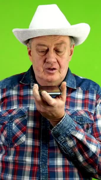 白いカウボーイのシニア男性は スピーカーフォンで音声メッセージを記録します スマートテクノロジーをソーシャルメディアコミュニケーション 音声コマンド メッセージングに使用します グリーン スクリーン クロマキー バーティカル — ストック動画