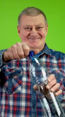 Kıdemli adam plastik şişeyi katlıyor ve geri dönüşüm için sıkıştırıyor. Olgun insan kolayca kurtulmak için plastik şişeyi sarmak için talimat verir. Yeşil ekran. Krom anahtar. Dikey.