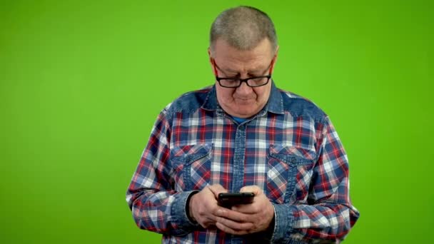 彼のスマートフォンでチャットする指の速いテキストメッセージを持つシニアマン 成熟した人は 携帯電話に2本の指でテキストを精力的にタイプし 通信を行います グリーン スクリーン クロマキー — ストック動画