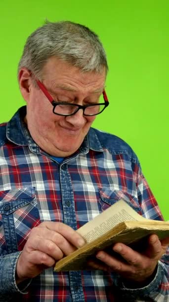 眼鏡のポジティブな上級男性は 本の情報を読んだり検索したりします 古文学の本のページを通して葉っぱを描く成熟した人 グリーン スクリーン クロマキー バーティカル — ストック動画