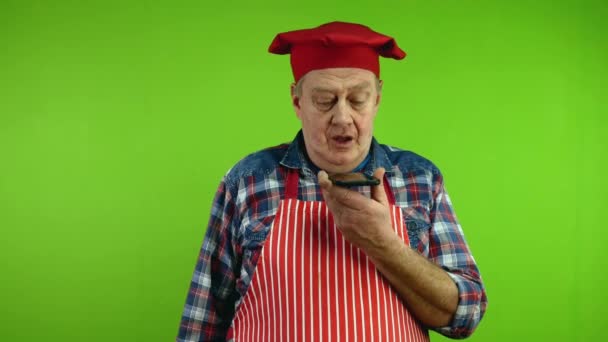Senior Kock Rött Förkläde Som Håller Smartphone Och Spelar Röstmeddelande — Stockvideo