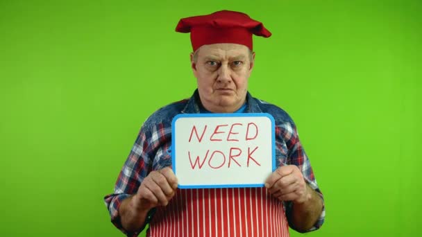 赤いエプロンのシニアシェフは 手の碑文が必要な仕事を保持しています 成熟した料理人は 失業と危機の時期に仕事を探しています グリーン スクリーン クロマキー — ストック動画