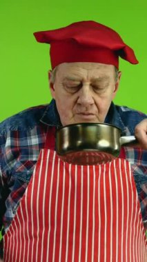 Kıdemli gurme şef güveçten yemek kokusu alıyor ve yemek kokusunun tadını çıkarıyor. Olgun aşçının taze yemek tatması zevk verir ve onaylar. Yeşil ekran. Krom anahtar. Dikey.