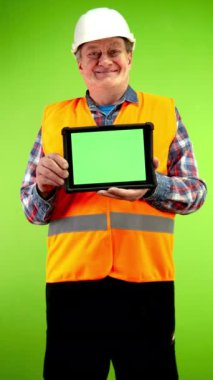 Yelek ve miğfer giyen kıdemli müteahhit boş reklam ekranlı tablet gösteriyor. Olgun işçi elinde kopyalama alanı olan yeşil ekran cihazı tutuyor. Yeşil ekran. Krom anahtar.