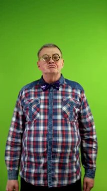 Garip gözlüklü bir adam kameraya bakıyor ve kollarını göğsünde kavuşturuyor. Olgun bir adamın kameraya bakıp poz vermesi eğlenceli. Yeşil ekran. Krom anahtar. Dikey.