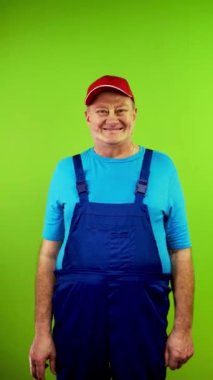 Tulumlu bir adam kameraya bakıyor, barış ya da zafer jesti gösteriyor. Olgun insan parmaklarıyla iki numarayı gösteriyor ve gülümsüyor. Yeşil ekran. Krom anahtar. Dikey.