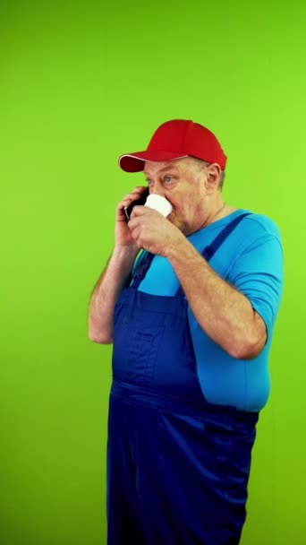 Starszy Mężczyzna Kombinezonie Mówi Smartfonie Pije Papierowego Szkła Dojrzała Osoba — Wideo stockowe