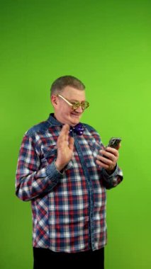 Komik gözlüklü tuhaf bir adam telefon kamerasıyla konuşuyor. Uzaktan iletişim için teknolojiyi kullanmak, uzaktan konuşmak. Yeşil ekran, krom anahtar. Dikey.