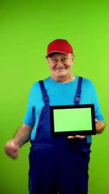 Önlüklü kıdemli tamirci boş reklam ekranlı tablet gösteriyor. Olgun işçi işaretleri ile yeşil ekranda fotokopi alanı olan bir cihaz. Yeşil ekran. Krom anahtar. Dikey.