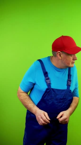 オーバーオールの修理担当者は 何も理解していません シニア ワーカーは周りを見回して握手する グリーンスクリーン クロマキー バーティカル — ストック動画