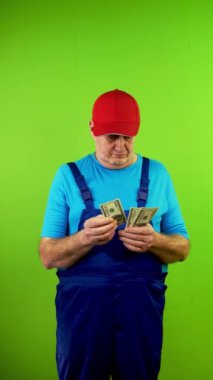 Kıdemli tamirci 100 dolarlık banknotları sayıyor ve öfkeyle iade ediyor. Ödeme görevlisinin anlaşmayı ya da teklifi reddetmesinden memnun değil. Yeşil ekran. Krom anahtar. Dikey.