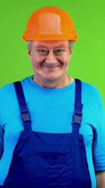 Önlüklü ve kasklı kıdemli işçi evet diyor, başını sallıyor ve kameraya bakıyor. Olumlu Olgun Tamirci biriyle zevkle aynı fikirde ve memnun. Yeşil ekran. Krom anahtar. Dikey.