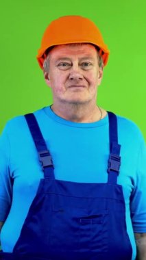 Önlüklü, kasklı, gülümseyen ve kollarını kavuşturan kıdemli bir işçi. Kasklı, mutlu ve gururlu bir tamirci. Yeşil ekran. Krom anahtar. Dikey.