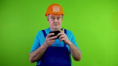 Tulum giymiş kıdemli bir işçi para dolu cüzdan gösteriyor. Gösteriler beni en iyi şekilde seçiyor. Olgun bir tamirci 100 dolarlık banknotlarla övünür. Yeşil Ekran. Krom anahtar.