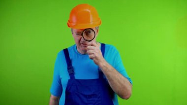 Elinde büyüteç tutan kıdemli işçi şaşırmış görünüyor. Olgun bir tamirci bir şeye bakar, gördüklerine çok şaşırır, asık suratlı bakar. Yeşil ekran. Krom anahtar.