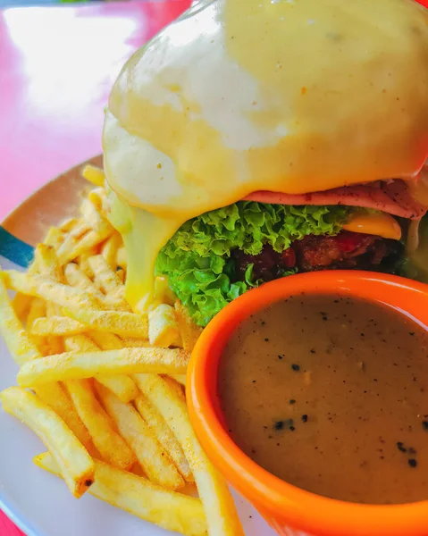 Beef cheeseburger with melted cheese served with black pepper sauce and fries.