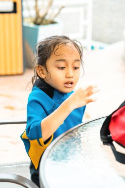 Küçük çocuk yüzme havuzunun yanında otururken ıslak yemek yiyor..