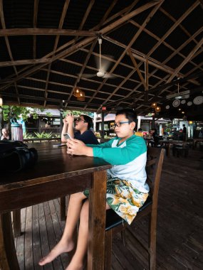 Redang, Malezya - 9 Mayıs 2022: Çocuklar masada oturuyor ve cep telefonu kullanıyorlar. Ciddi görünüyorsun..