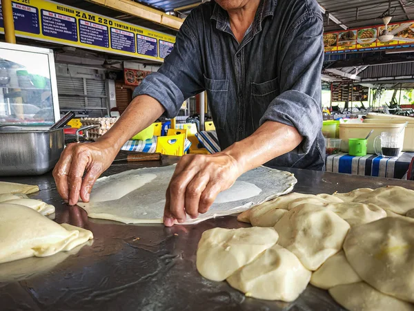 Selangor, Malaysia - June 4, 2022 Making Roti Parata or Roti canai with curry sauce - popular Malaysian breakfast