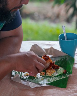 Malezya 'daki çeltik tarlasının yanında muz yapraklarıyla sarılmış bir adam Nasi Lemak yiyor..