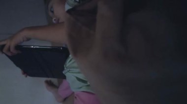  Odada yatakta yatarken tablet kullanan küçük bir kız. Dikey video. Yavaş çekim