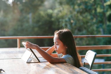 Dışarıda güneş doğarken tablet bilgisayar kullanan küçük bir kız..