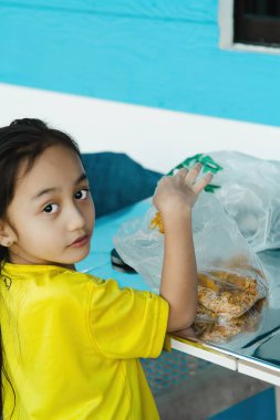 Masadaki plastik torbadan kızarmış yiyecek alıyorum. Asyalı çocuk kameraya bakıyor..