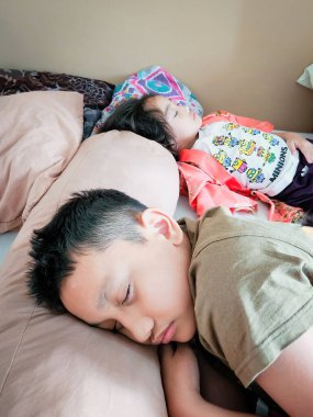 Bangi, Malezya - 7 Haziran 2022 Kardeşler yatakta birlikte uyuyorlar. Büyük abi ve küçük kız kardeş..