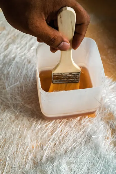 Boya fırçasını cam elyaf çözeltisinin içine daldırıyorum. Fiberglas çarşafın üstündeki bir kapta..