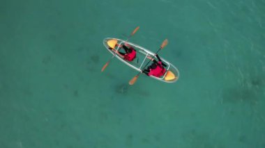 Denizde şeffaf bir teknede kano süren iki kişinin baş aşağı görüntüsü. 4K