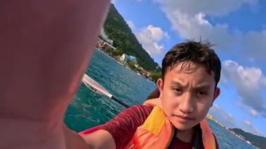 Terengganu, Malezya, 16 Mart 2023 Pulau Perhentian Kecil 'de tatildeyken bir çocuk kendi fotoğrafını çekiyor. Babasıyla birlikte bir kanoda..