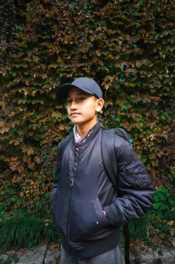 Sarmaşık duvar arka tarafta açık hava kıyafeti giyen genç bir çocuk dik dik bakıyor..