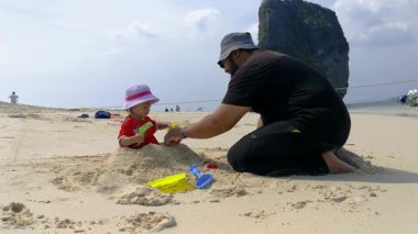 Genç kıza kumdan kale inşaatında yardım eden adam.