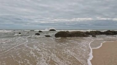 Deniz dalgaları kayalık kumlu kumsal bulutlu bir gün. Kameraya el salla. Yüksek kalite 4k görüntü