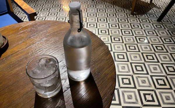 一个装有冰块和透明玻璃瓶的透明玻璃杯 装有冰冷的矿泉水 放在木制桌子上 用它解渴 — 图库照片