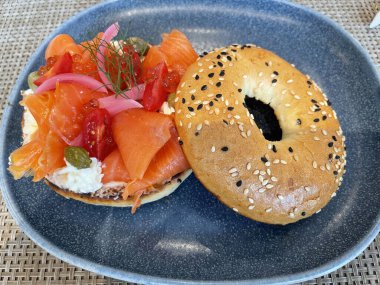 Seçici odak noktası, füme somon, ıspanak, kırmızı soğan, domates, avokado ve krem peynirli lezzetli simit. Hafif bulanık parçalı seçici odak