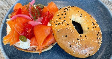 Seçici odak noktası, füme somon, ıspanak, kırmızı soğan, domates, avokado ve krem peynirli lezzetli simit. Hafif bulanık parçalı seçici odak