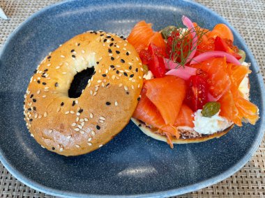 Seçici odak noktası, füme somon, ıspanak, kırmızı soğan, domates, avokado ve krem peynirli lezzetli simit. Hafif bulanık parçalı seçici odak