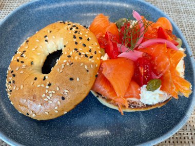 Seçici odak noktası, füme somon, ıspanak, kırmızı soğan, domates, avokado ve krem peynirli lezzetli simit. Hafif bulanık parçalı seçici odak