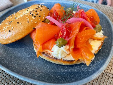 Seçici odak noktası, füme somon, ıspanak, kırmızı soğan, domates, avokado ve krem peynirli lezzetli simit. Hafif bulanık parçalı seçici odak