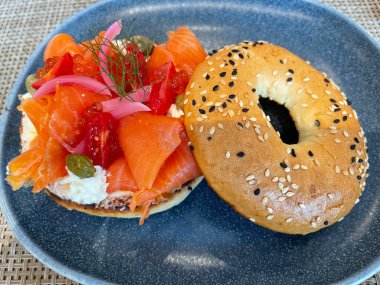 Seçici odak noktası, füme somon, ıspanak, kırmızı soğan, domates, avokado ve krem peynirli lezzetli simit. Hafif bulanık parçalı seçici odak