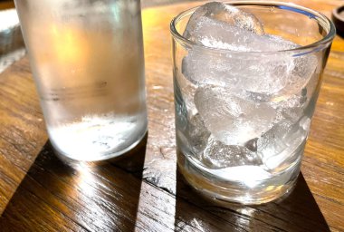 Seçici odak, buzla dolu berrak bir bardak ve temiz bir cam şişe soğuk maden suyunu ahşap masaya koyar, susuzluğu gidermek için su kullanır.