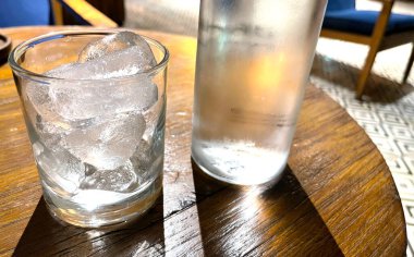 Seçici odak, buzla dolu berrak bir bardak ve temiz bir cam şişe soğuk maden suyunu ahşap masaya koyar, susuzluğu gidermek için su kullanır.