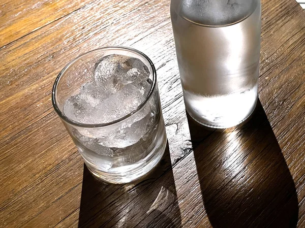 選択的フォーカス 氷とクリアガラスボトルで満たされた透明なガラスは 冷たいミネラルウォーターを木製のテーブルの上に座っている 喉の渇きを癒すための水の使用 — ストック写真